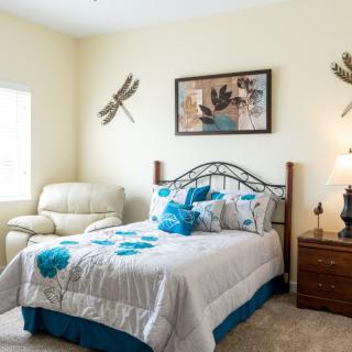 A cozy bedroom with dragonfly-themed decor, featuring a comfortable armchair and a well-made bed.