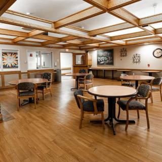 A spacious dining area with wooden floors, featuring several tables and chairs, decorated with artwork on the walls.
