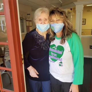 Two people wearing masks, standing side by side and smiling indoors.