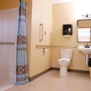 An accessible bathroom featuring a toilet, sink, and shower with grab bars for added safety.