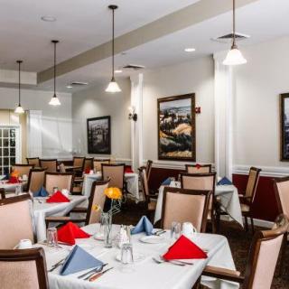 A well-lit dining area with neatly arranged tables, adorned with colorful napkins and elegant chairs, surrounded by framed artwork.
