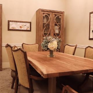 A cozy dining room with a wooden table and upholstered chairs, featuring a decorative cabinet in the background.