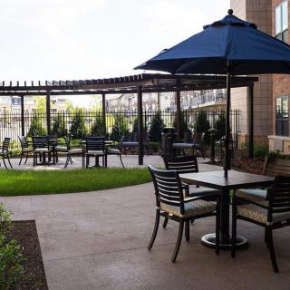 A peaceful outdoor patio area with tables, chairs, and umbrellas set against a backdrop of lush greenery.