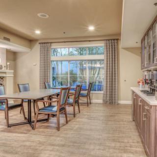 A modern dining room with a wooden table and chairs, adjacent to a kitchen area with cabinetry.