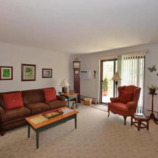 A cozy living room with a sofa, armchair, and coffee table, featuring artwork on the walls and a sliding glass door leading outside.