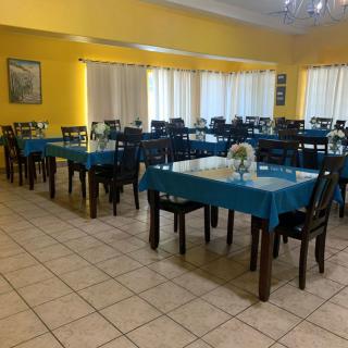 An empty dining room with arranged tables and chairs, featuring yellow walls and tiled flooring.