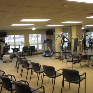 A fitness center with exercise equipment and chairs arranged for a meeting.