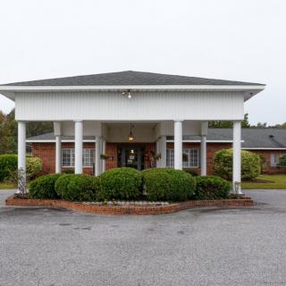 A building with a covered entrance supported by columns and surrounded by landscaped greenery.