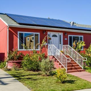 A charming red house with solar panels and a well-maintained garden.