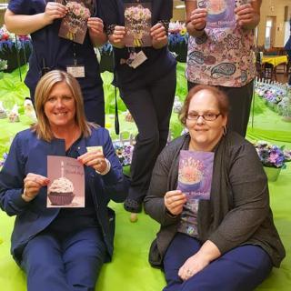 A group of people smiling and holding cards indoors during an event.