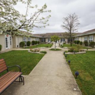 A serene courtyard with a central pathway, green lawns, and a bench surrounded by buildings.