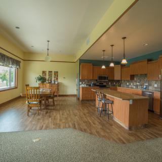 An open-concept kitchen and dining area featuring light wood cabinets, an island with bar stools, and a large window providing natural light.