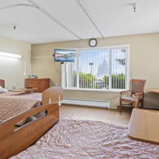 A hospital room featuring two patient beds, a window with a view, and basic furniture.
