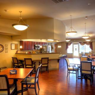 A cozy dining room with wooden tables and chairs, featuring a bar area and warm lighting.