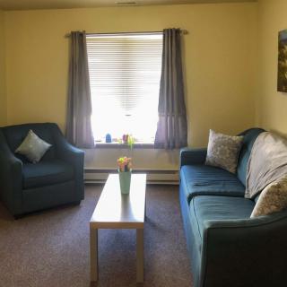 A cozy living room with a sofa, armchair, and coffee table by a window with curtains.