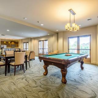 A spacious recreational room featuring a pool table and dining area, illuminated by natural light through large windows.