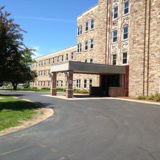A stone building with a covered entrance and a surrounding driveway, set against a clear blue sky.