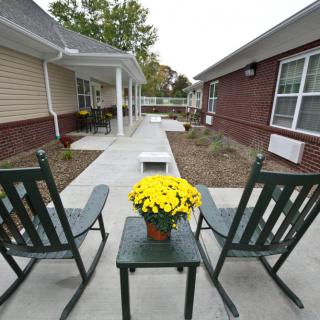 Two rocking chairs on a patio facing a walkway, with a table holding a pot of yellow flowers.