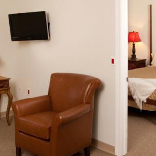 A cozy hotel room with a leather chair, wall-mounted television, and a glimpse into the adjacent bedroom.