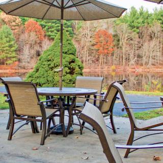 A patio setup with chairs and an umbrella overlooking a serene autumn landscape by a lake.