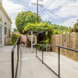 A backyard patio with a ramp, surrounded by a wooden fence and garden foliage.