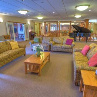 A spacious living area featuring comfortable sofas, a coffee table with a plant, and a grand piano in the background.
