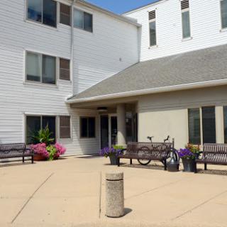 A sunny day at the entrance of a modern building, surrounded by colorful flowers and benches.