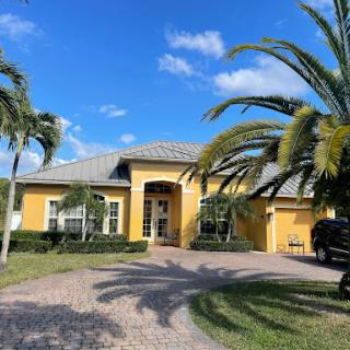 A beautiful yellow house surrounded by palm trees under a clear blue sky.