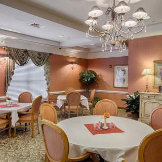 An elegant dining room with round tables, cushioned chairs, and a chandelier.