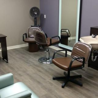 An empty hair salon with two chairs, a large mirror, and a sink.