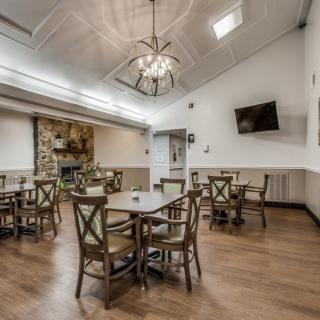 A cozy dining room with wooden flooring, round tables, chairs, and a chandelier.