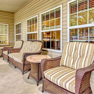 A cozy patio area with wicker chairs featuring striped cushions and a small side table, set against a backdrop of windows.