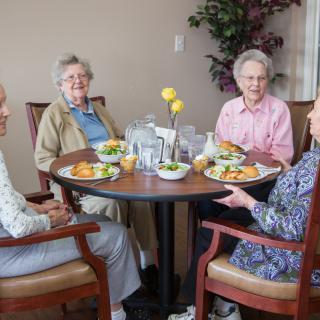 Four elderly women enjoying a meal together at a dining table.