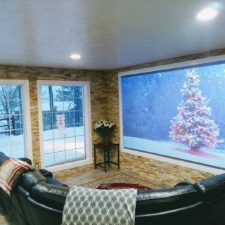 A cozy living room with large windows overlooking a snowy scene, featuring a decorated Christmas tree and comfortable seating.