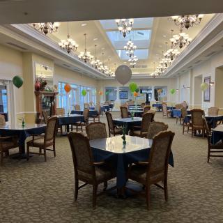 A spacious dining area with elegantly arranged tables and chairs, adorned with colorful balloons and illuminated by chandeliers.