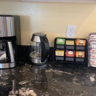 A kitchen counter with a coffee maker, electric kettle, assorted tea bags, and sugar packets.