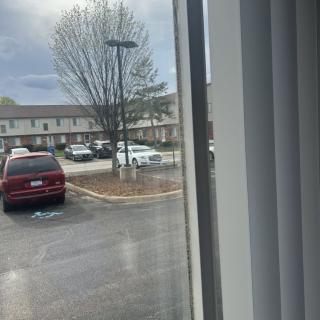 View from a window overlooking a parking lot with several cars under an overcast sky.