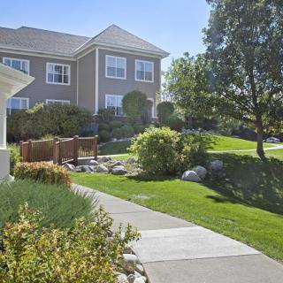 A sunny day in a residential neighborhood with a house, landscaped garden, and pathway.