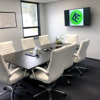 A modern conference room equipped with a large meeting table, white chairs, and a screen displaying a logo.