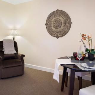 A cozy living room with an armchair, a lamp, and a dining table adorned with decorative items.
