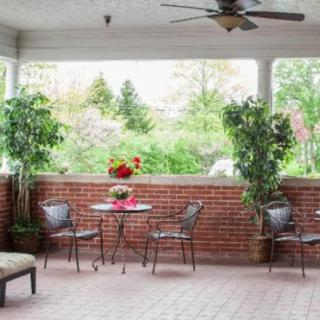A cozy patio area with a table and chairs, surrounded by lush greenery and a brick wall.