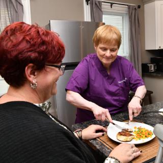 A caregiver serving a delicious meal to a smiling client in a cozy kitchen.