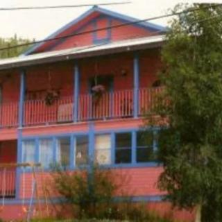 A colorful two-story house with blue accents and a balcony, surrounded by greenery.