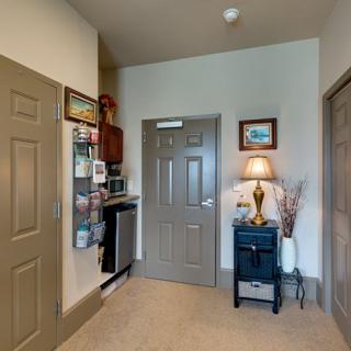 A cozy interior with a lamp on a small table, artwork on the wall, and multiple doors.