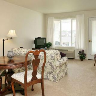 A cozy living room featuring a wooden table with chairs, a plush sofa, a television, and a standing lamp by the window.