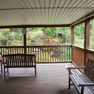 A peaceful covered porch with wooden seating overlooking a lush garden.