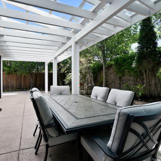A spacious backyard patio with a pergola, featuring a large dining table and comfortable chairs.