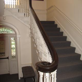 A classic interior staircase with a wooden banister and carpeted steps.