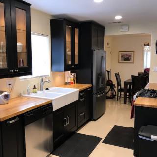 A modern kitchen with black cabinets and wooden countertops, leading into a dining area.