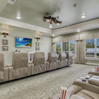 A luxurious home theater with comfortable seating, a large TV screen, and elegant chandeliers.